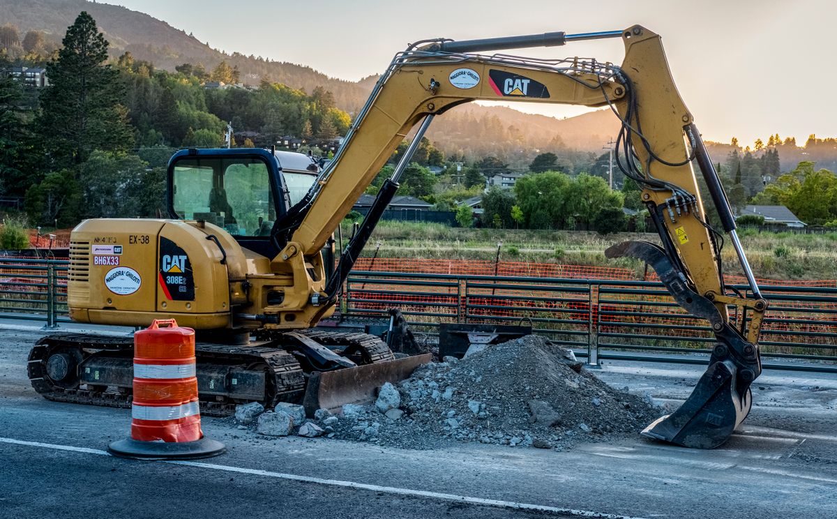 Excavator breaking and clearing a driveway at a job site